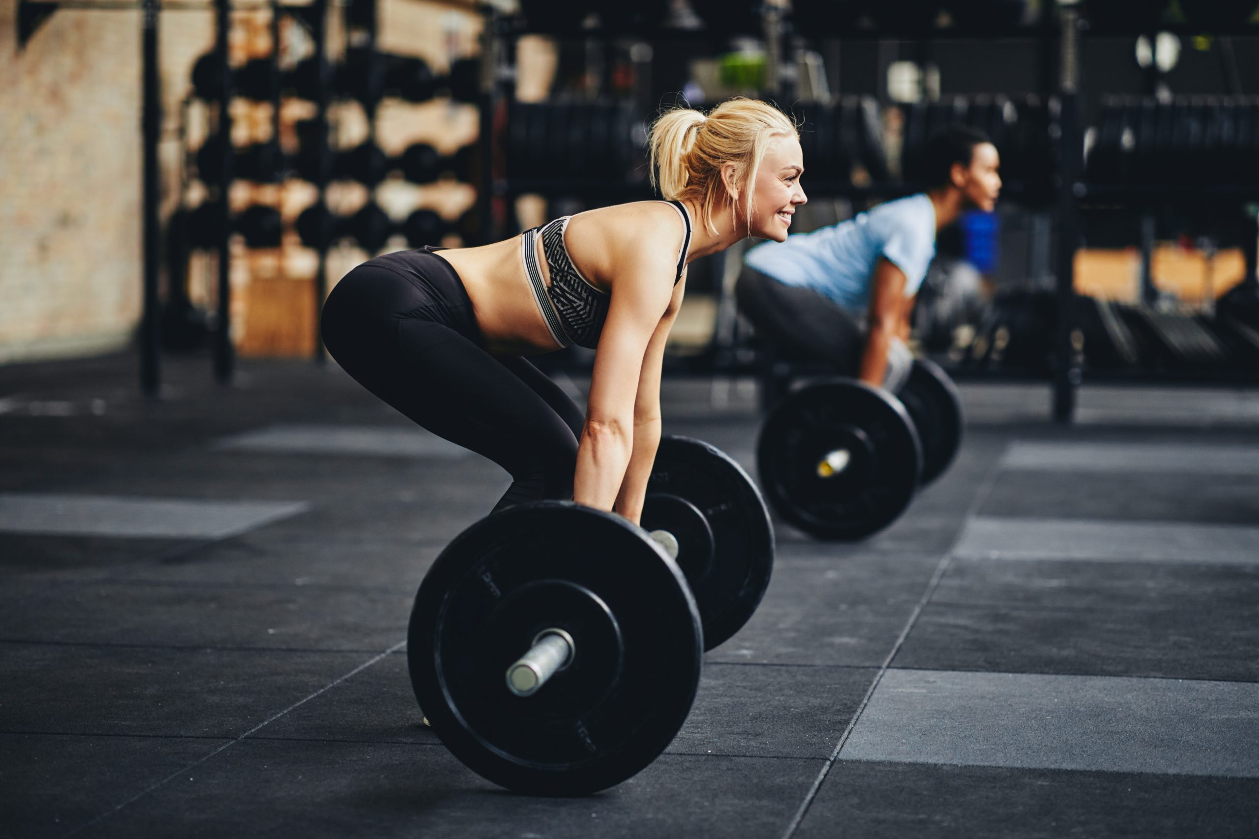 Fit young woman in sportswear smiling while preparing to lift barbells during a weight lifting class at the gym